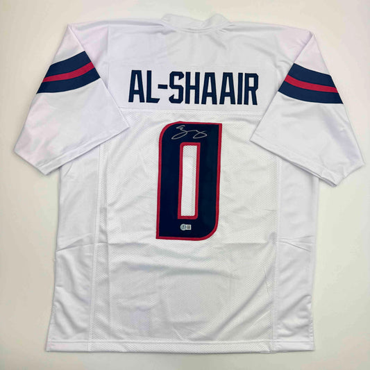 White football jersey with navy and red striped sleeves, displaying "AL-SHAAIR" and number "0" with signature, flat lay view.