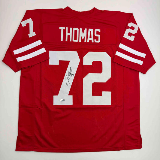 Red Wisconsin college football jersey number 12 with "THOMAS" nameplate, displayed flat with visible autograph on front.
