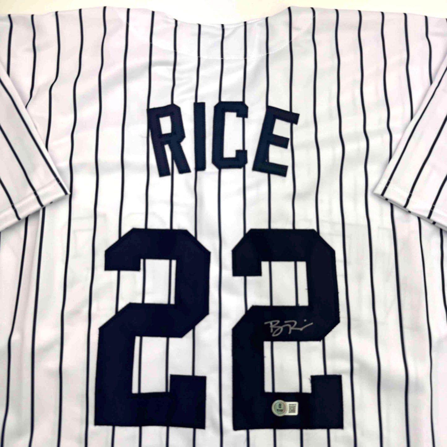White pinstriped baseball jersey with "RICE" and number "28" in navy blue, displayed flat with visible signature and authentication sticker.