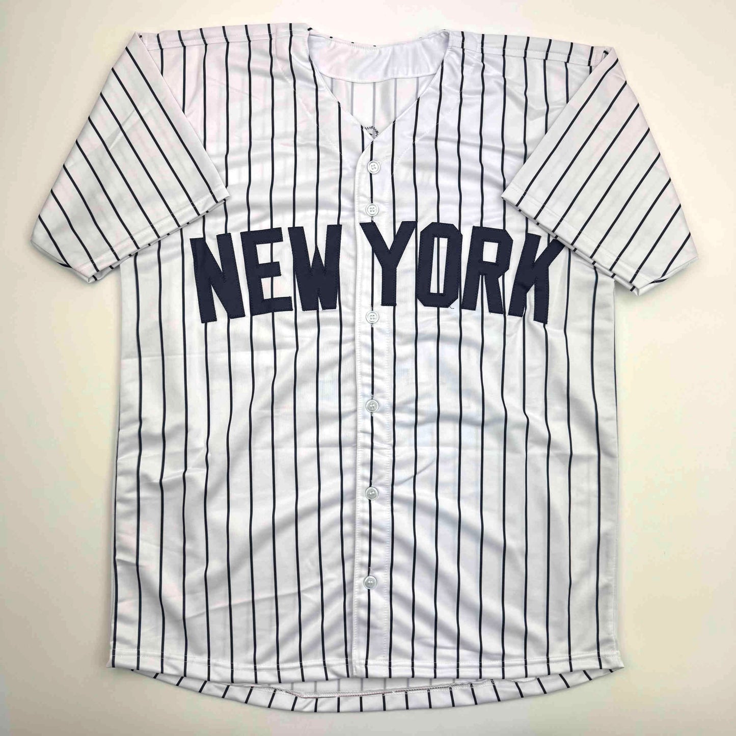 White pinstriped New York baseball jersey with navy blue vertical stripes and "NEW YORK" text across chest, displayed flat against cream background.