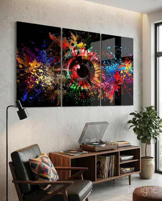 Three-panel colorful glass wall art with abstract eye design and vibrant paint splatters displayed above mid-century furniture in modern interior.