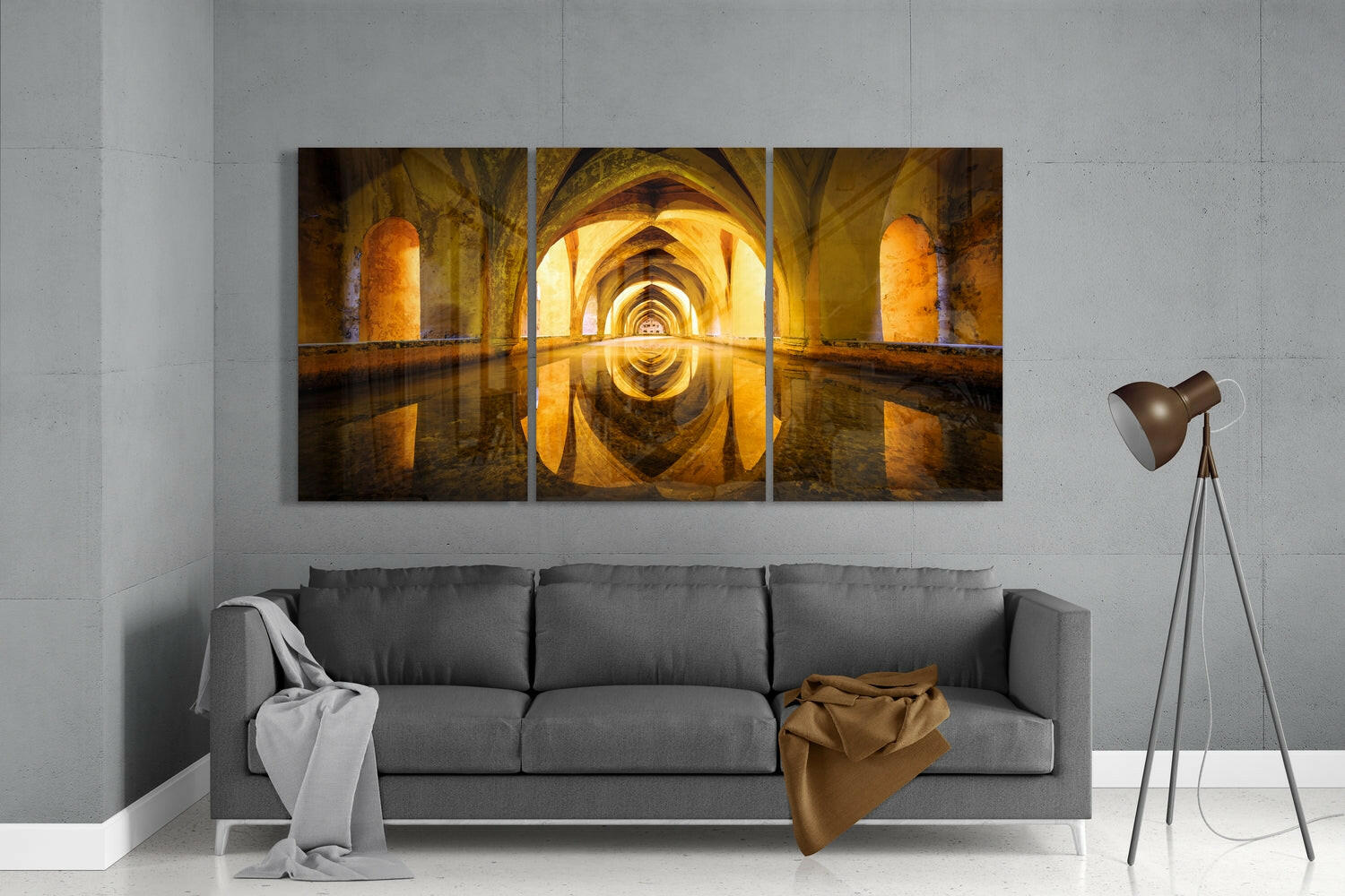 Three-panel glass wall art depicting a symmetrical golden-lit arched stone corridor with water reflection, displayed above a gray sofa in a modern living room.