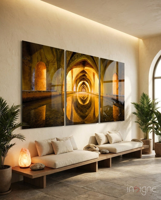 Three-panel glass wall art displaying golden-lit arched corridor with water reflection, installed above cream sofa in bright minimalist interior.