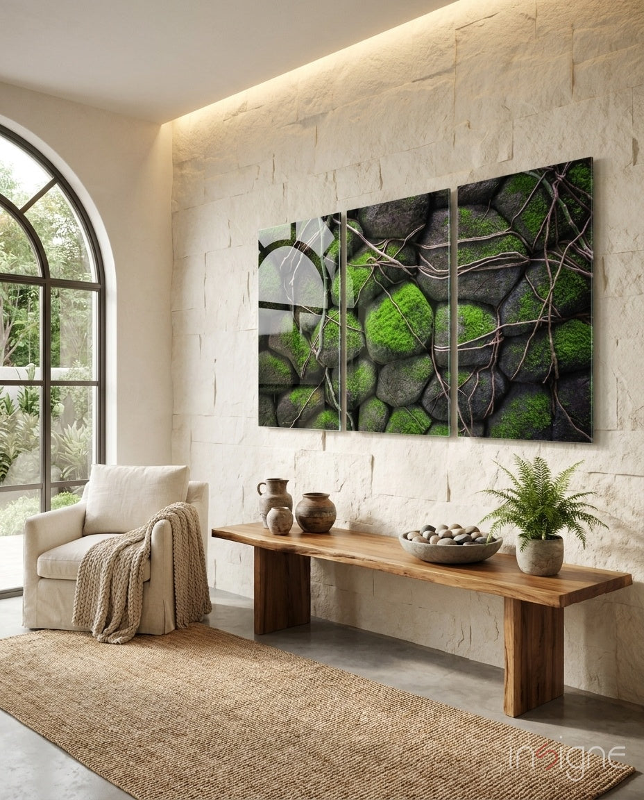 Triptych glass wall art featuring moss-covered stones and brown vines displayed above wooden bench in minimalist interior.
