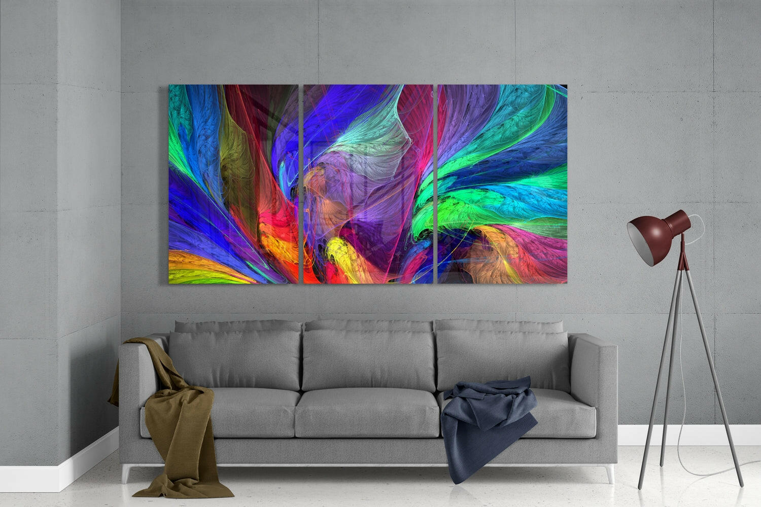 Colorful abstract glass wall art triptych displaying swirling blue, green, red, and yellow brushstrokes hung above gray sofa in modern interior.