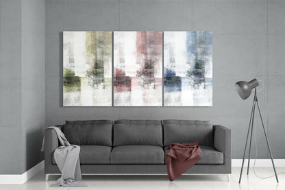 Modern living room with gray sofa displaying three pastel glass wall art panels in yellow, pink, and blue tones above it.