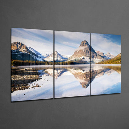 Three-panel glass wall art displaying snow-capped mountains reflected in a calm alpine lake surrounded by evergreen forest.