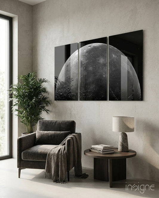 Multi-panel black glass wall art displaying a detailed grayscale moon surface, installed above a charcoal armchair in a minimalist interior.