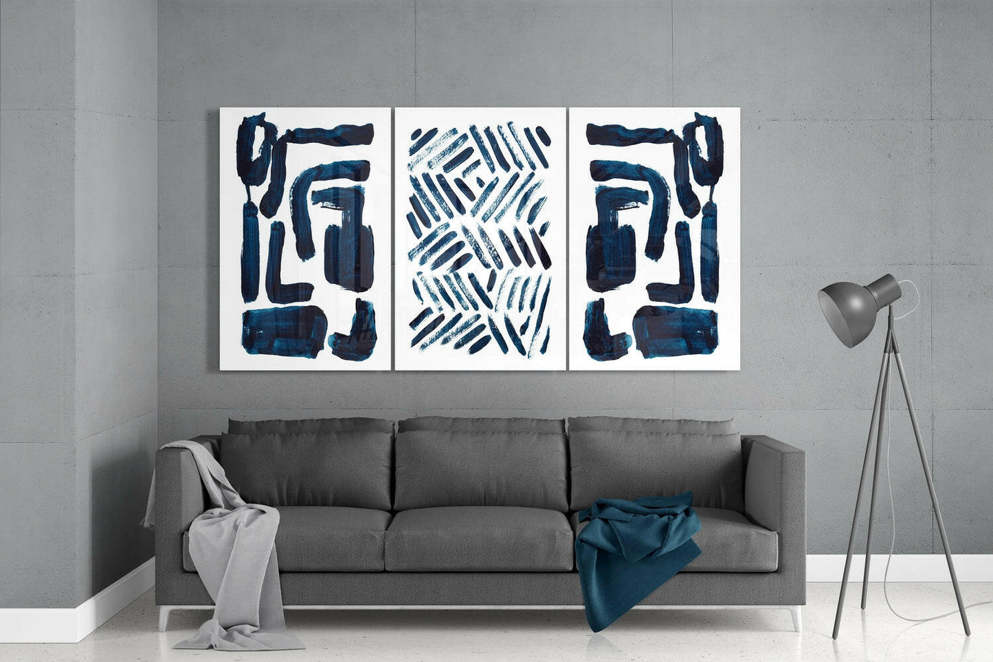 Three framed glass panels with navy blue abstract brushstrokes and geometric patterns hung above a gray sofa in a minimalist living room.