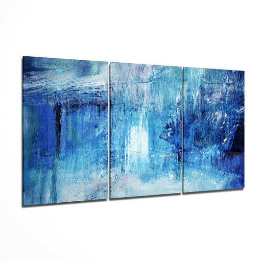 Three-panel abstract glass wall art displaying layered blue and white brushstrokes in varying intensities, angled perspective view.