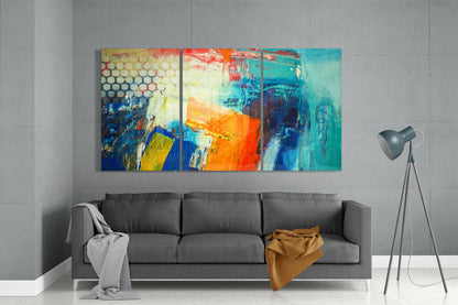Modern living room with gray sofa displaying three-panel abstract glass art above, featuring vibrant turquoise, orange, blue, and yellow brushstrokes.