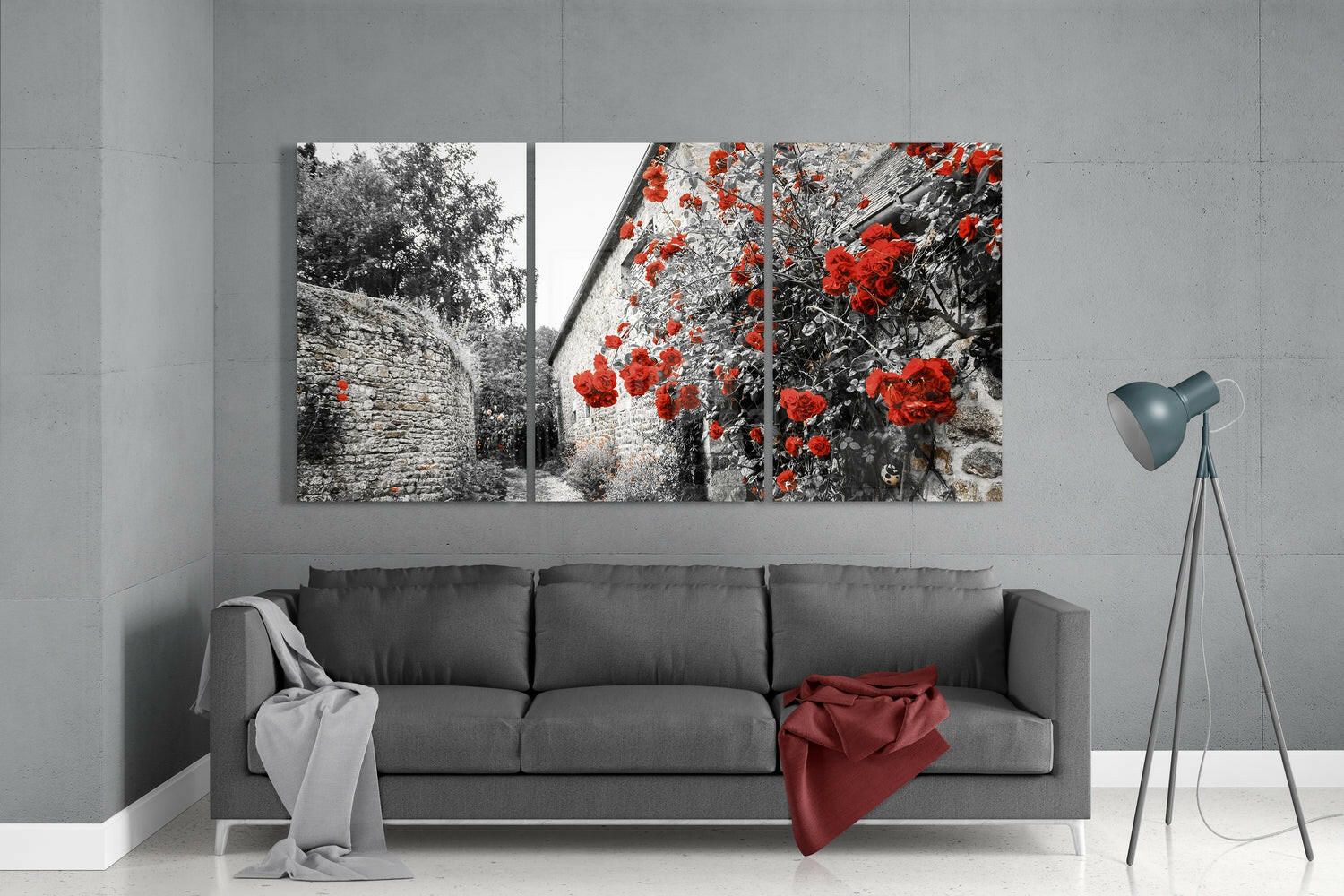 Three-panel glass wall art displaying black and white stone architecture with vibrant red flowers, hung above gray sofa in modern living room.