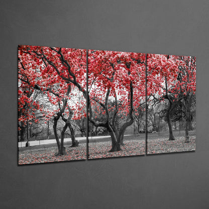 Multi-panel glass wall art displaying a park lined with black-branched trees bearing vibrant red blossoms against a desaturated grey landscape.