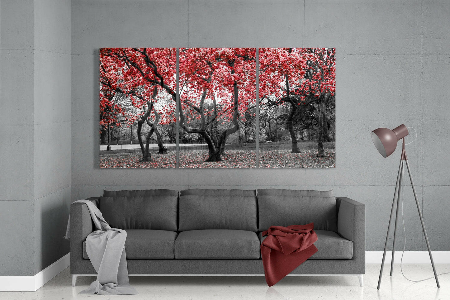 Three-panel glass wall art depicting black tree trunks with bright red foliage displayed above gray sofa in modern living room.