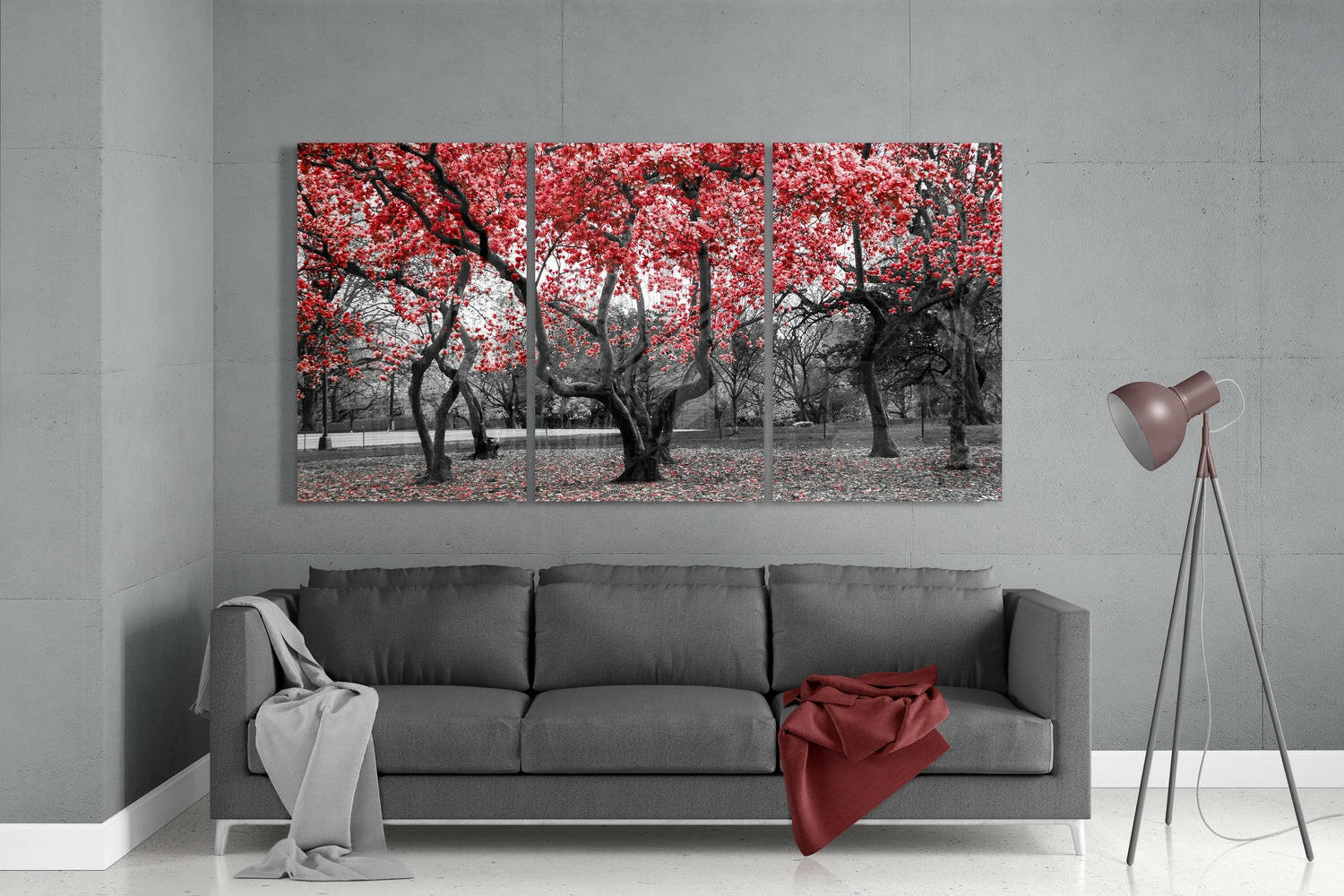 Three-panel glass wall art depicting black tree trunks with bright red foliage displayed above gray sofa in modern living room.