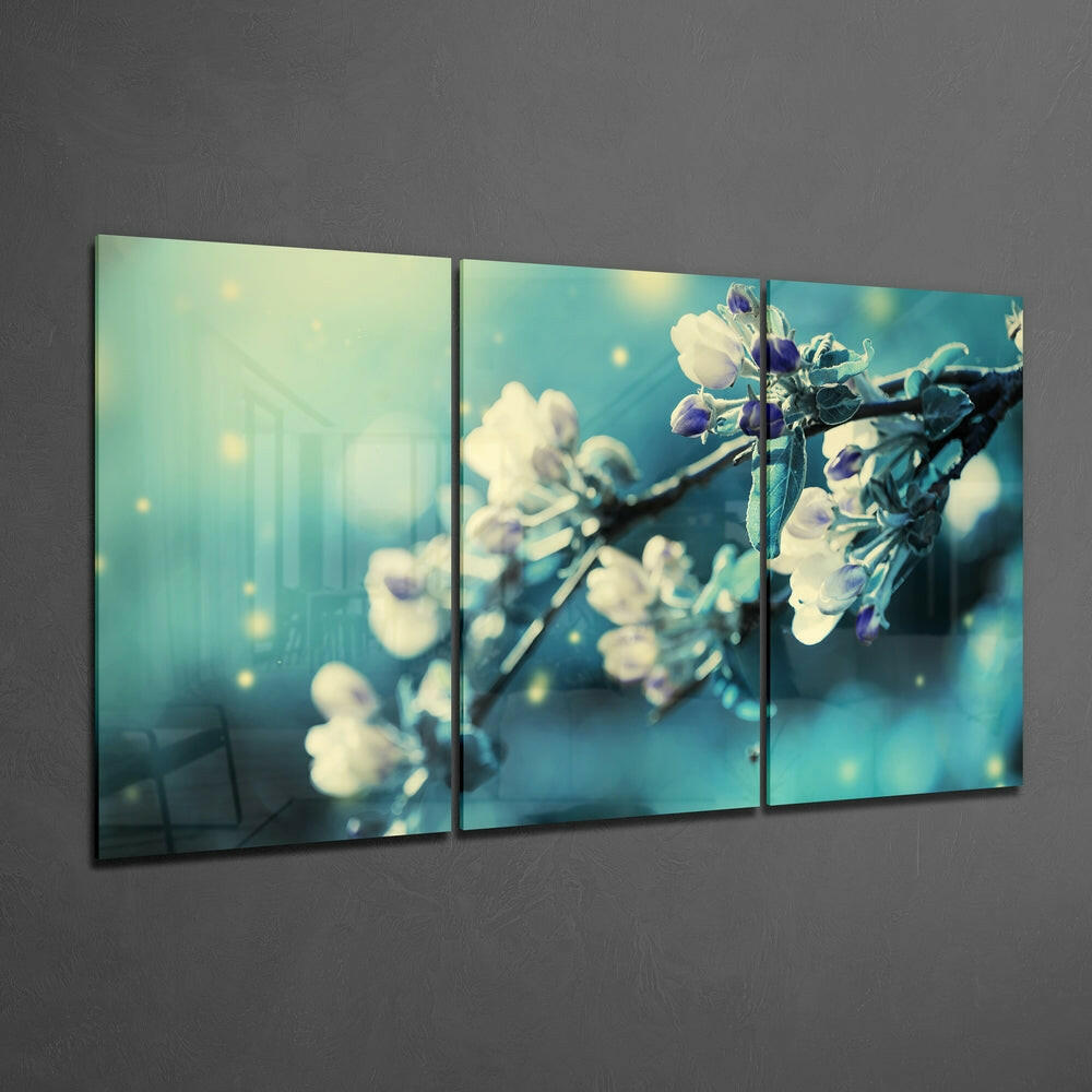 Three-panel glass wall art displaying delicate white and purple flowers on branches against a turquoise and yellow bokeh background.