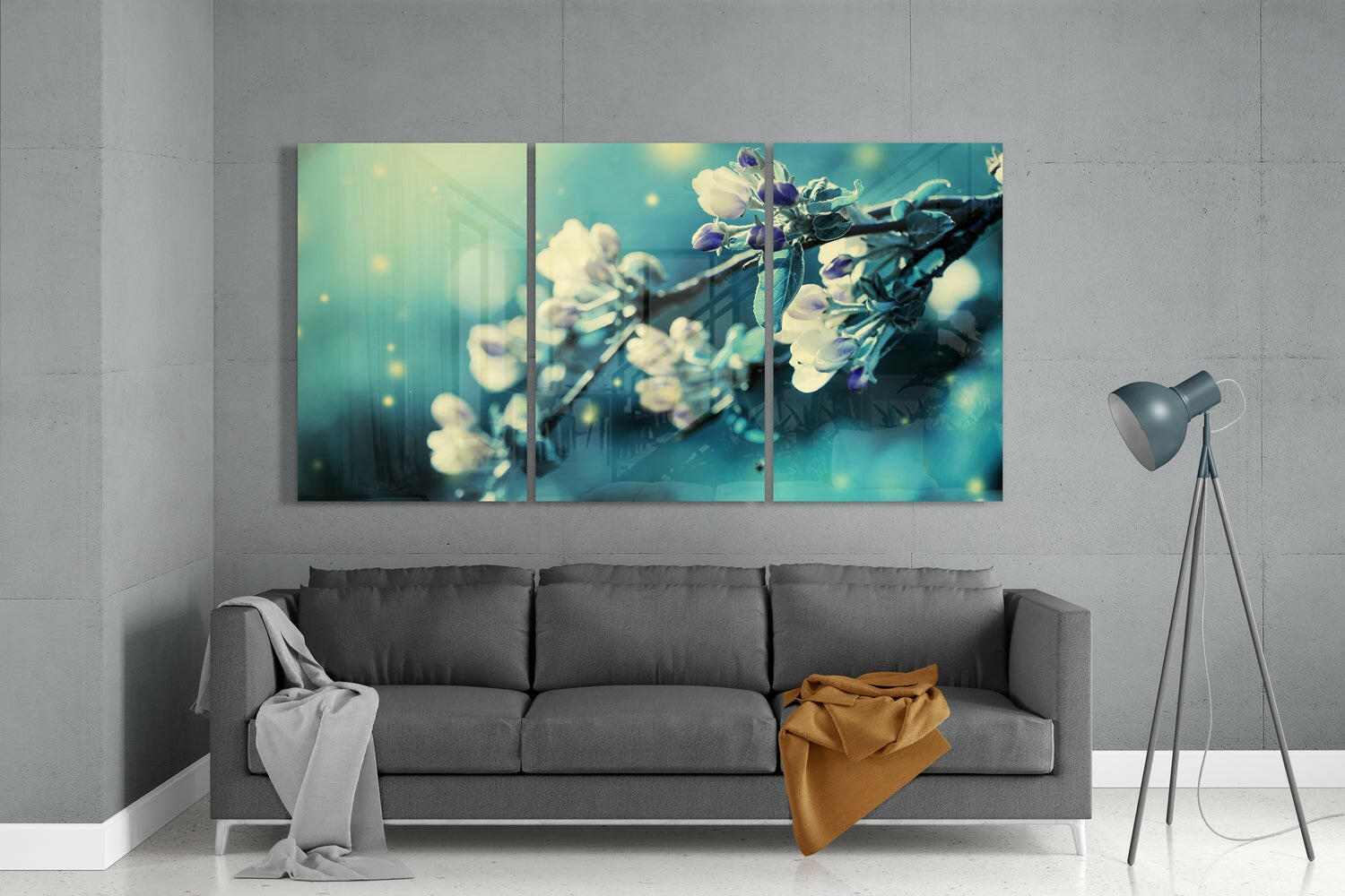 Three-panel teal and cream glass wall art depicting delicate white flowers on branches, displayed above a gray sofa in a modern living room.