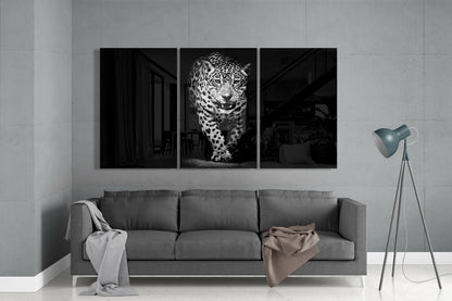 Three-panel black and white glass wall art displaying a leopard in the center panel, mounted above a gray sofa in a minimalist interior.