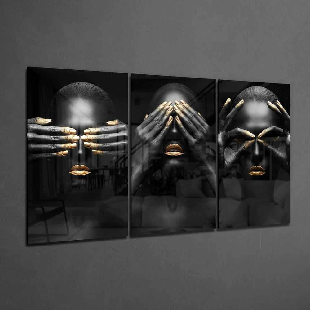 Three-panel glass art displaying stylized black and gold figures with covered faces against gray wall.