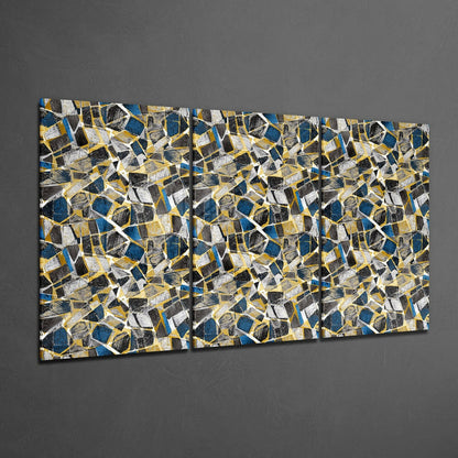 Three-panel glass wall art with abstract geometric pattern in navy blue, gold, white, and black shapes displayed on gray wall.