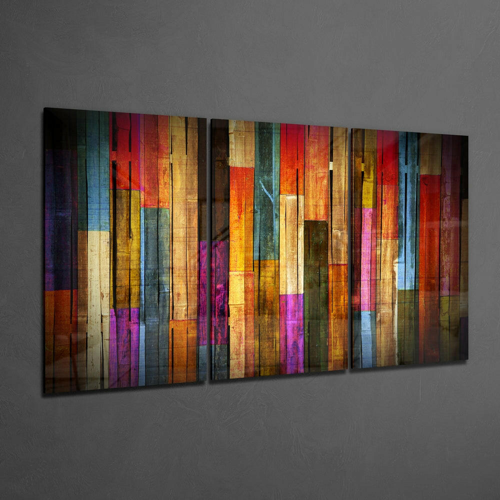 Colorful vertical striped glass wall art panel mounted on gray wall, featuring red, blue, yellow, orange, purple, and brown painted wooden planks.