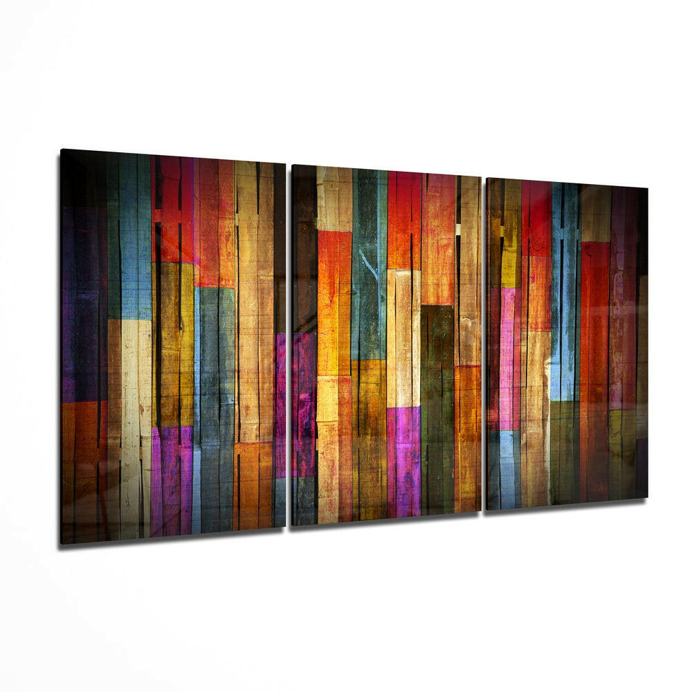Three-panel glass wall art displaying vertical painted wood strips in vibrant reds, blues, yellows, purples, and earth tones, angled perspective view.