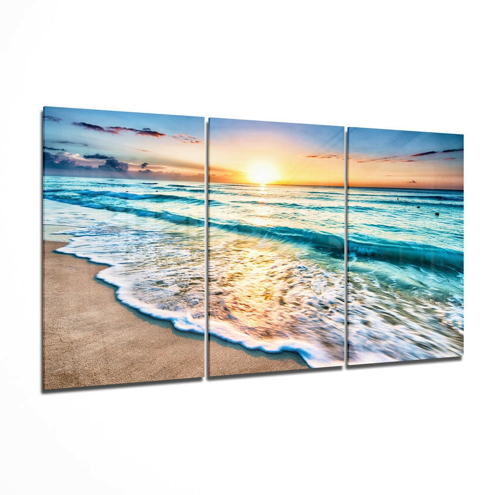 Three-panel glass wall art displaying a beach sunset with turquoise waves, golden light, and sandy shore in perspective view.