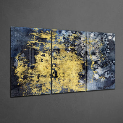 Three-panel triptych glass wall art with distressed yellow and dark blue abstract texture mounted on gray wall.