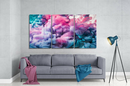 Three-panel glass wall art displaying swirling pastel clouds in pink, purple, blue, and white tones, installed above a gray sofa in a modern living room setting.