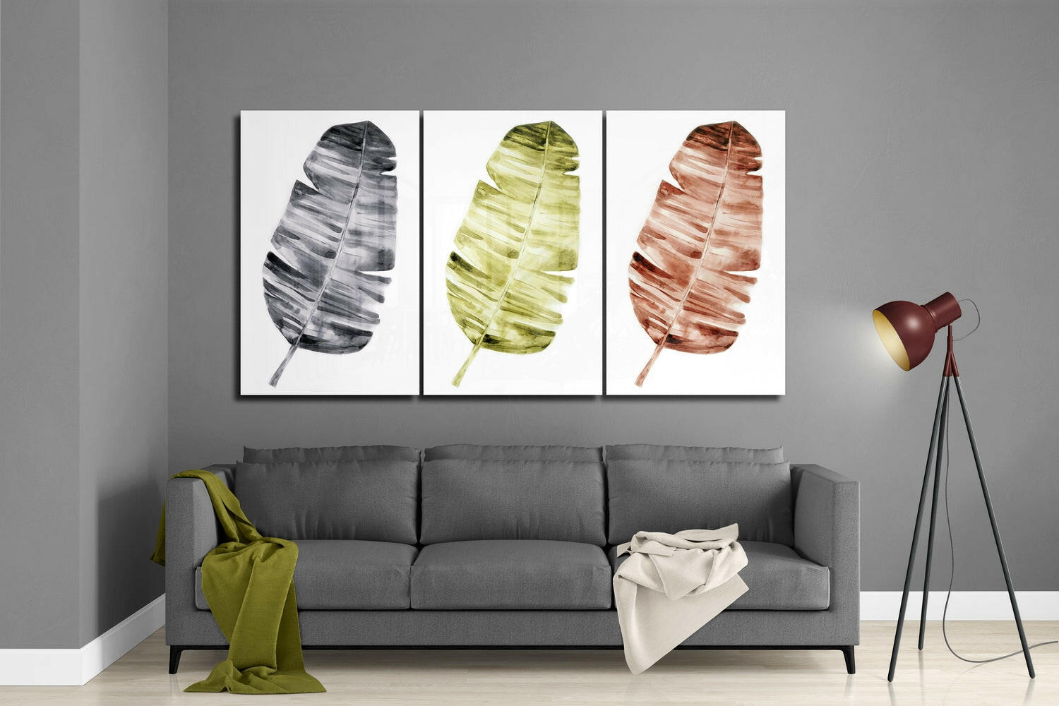 Three framed glass leaf artworks in black, green, and rust tones displayed above a gray sofa in a modern living room.