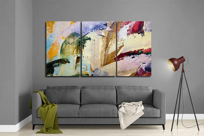 Three-panel abstract glass wall art with colorful brushstrokes in yellow, blue, red, and green displayed above gray sofa in modern living room.