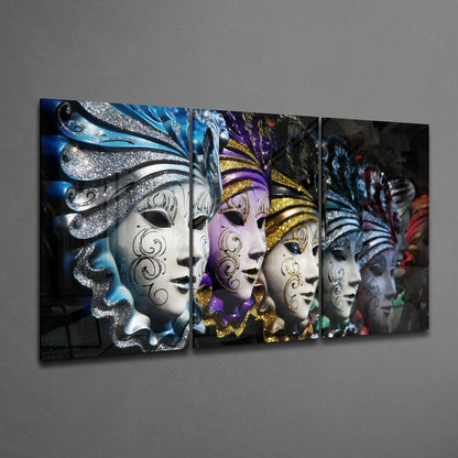 Multi-panel glass wall art displaying five ornate Venetian masks in blue, purple, gold, and white with decorative feathers and scrollwork, mounted horizontally on gray wall.