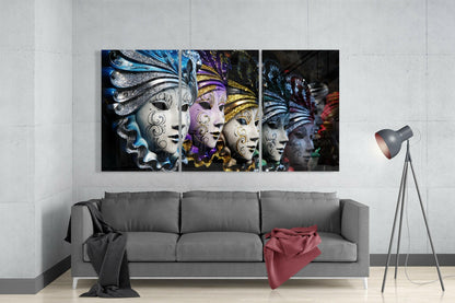 Triptych glass wall art displaying ornate Venetian masks with blue, purple, and gold embellishments mounted above gray sofa in modern living room.