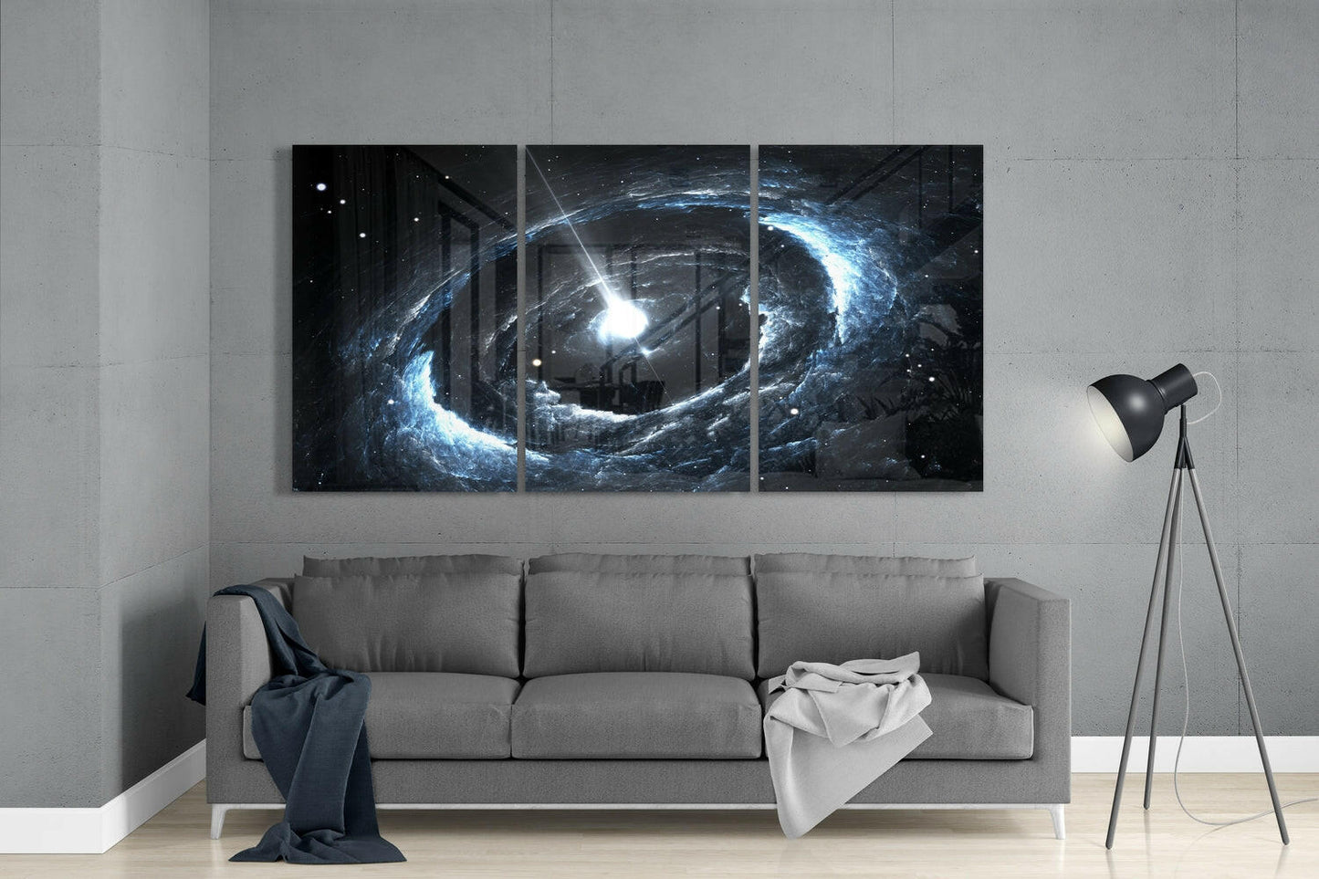 Three-panel glass wall art displaying a blue and white cosmic spiral with bright central light, installed above a gray sofa in a minimalist room.