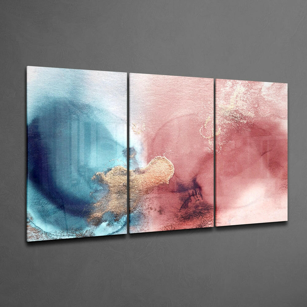 Three-panel glass wall art displaying abstract watercolor transitions from blue and teal on the left to coral and rose pink on the right, with gold metallic accents throughout.