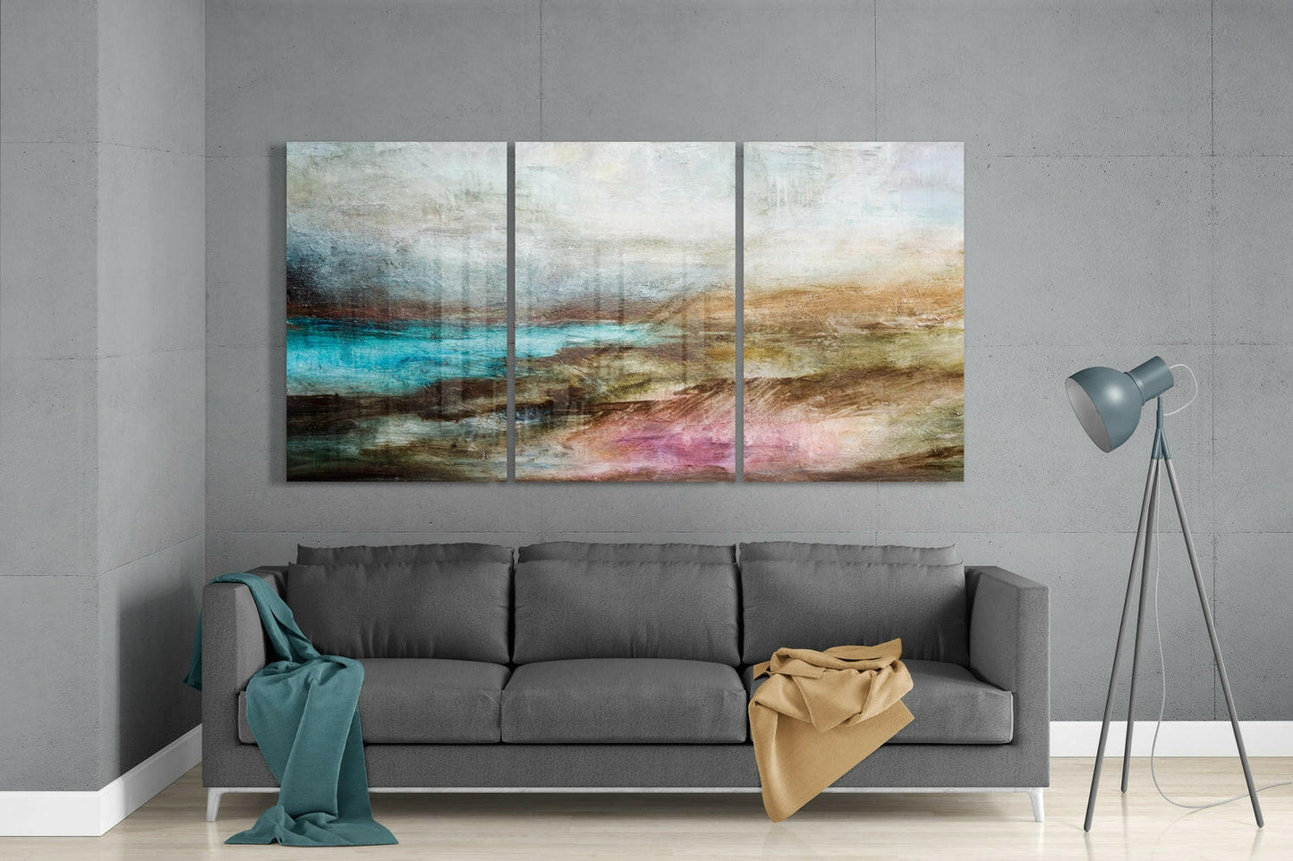 Three-panel abstract glass art above gray sofa displays layered landscape with turquoise, brown, and pink tones.