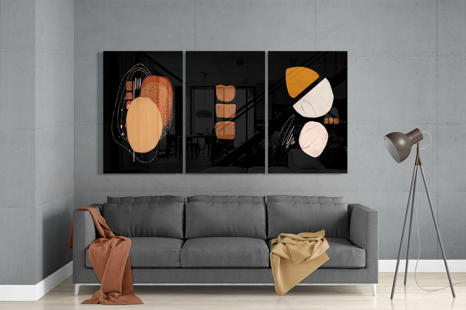 Three black glass panels with abstract geometric shapes in orange, cream, and white hung above a gray sofa in a modern living room.
