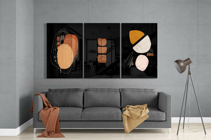 Three black glass panels with abstract geometric shapes in orange, cream, and white hung above a gray sofa in a modern living room.