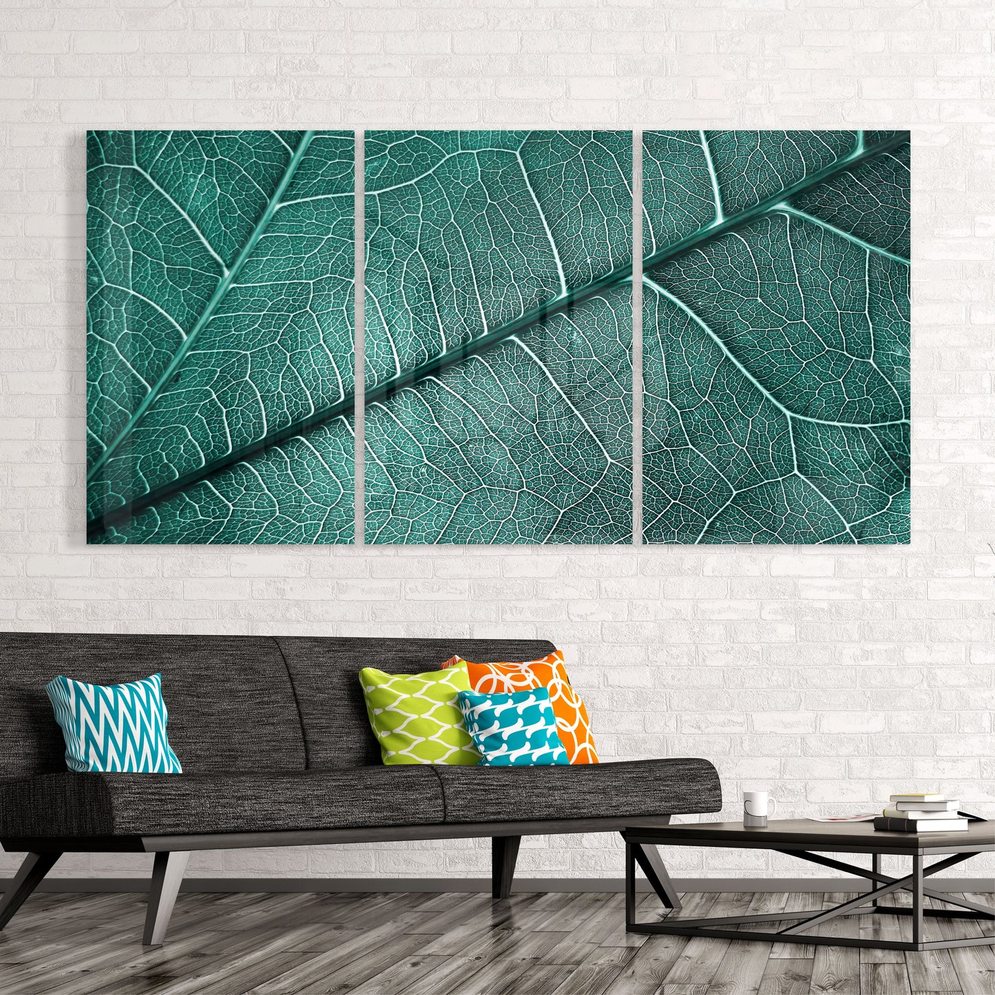 Three-panel green leaf vein glass art installed above a gray sofa with colorful patterned pillows in a modern living room.