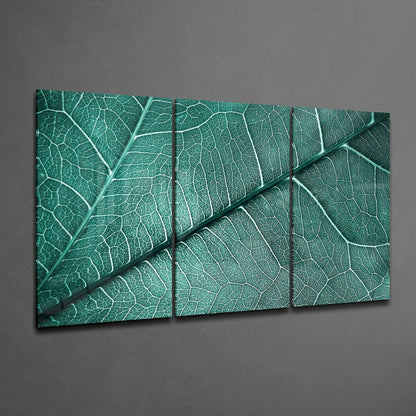 Three-panel teal glass wall art displaying close-up leaf vein details mounted on gray wall.