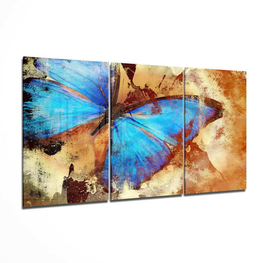 Three-panel glass wall art displaying blue morpho butterflies with distressed rust and gold tones on an angled perspective view.