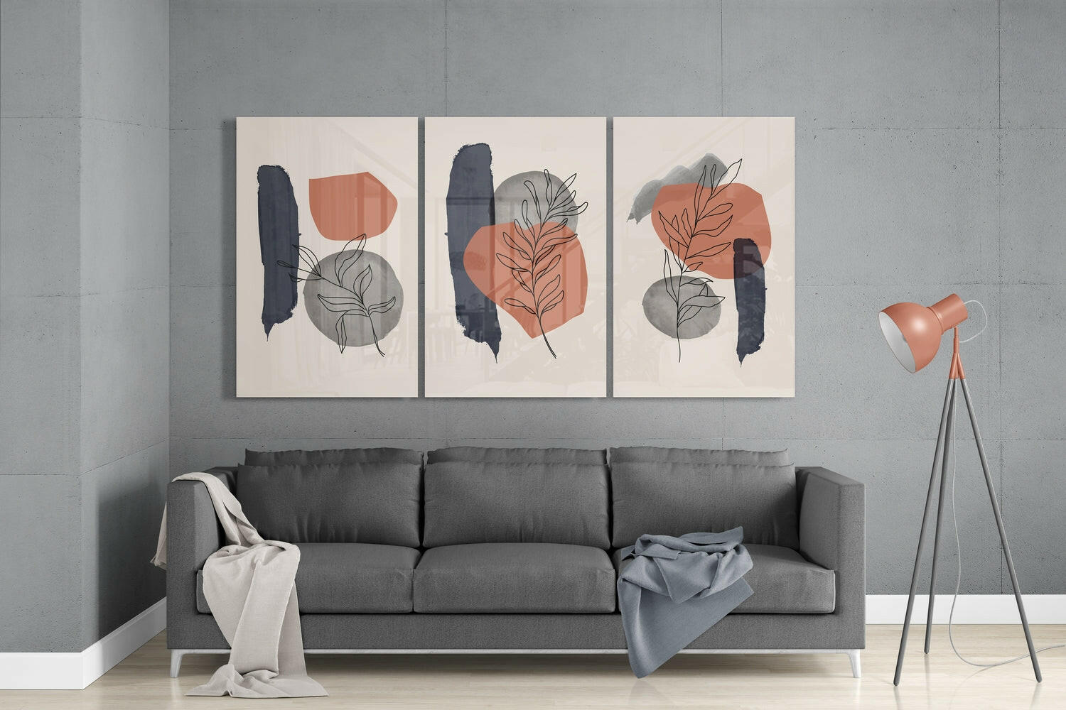 Three abstract glass wall panels with cream backgrounds displaying navy brushstrokes, terracotta and gray geometric shapes, and botanical line drawings hung above a gray sofa.