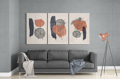 Three abstract glass wall panels with cream backgrounds displaying navy brushstrokes, terracotta and gray geometric shapes, and botanical line drawings hung above a gray sofa.