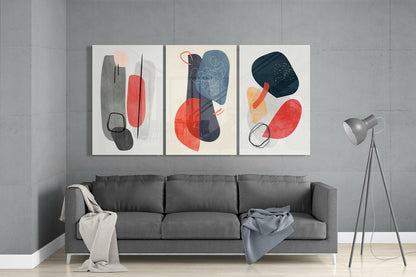 Three framed abstract glass wall arts with geometric shapes in red, gray, and navy blue displayed above a gray sofa in a modern living room.