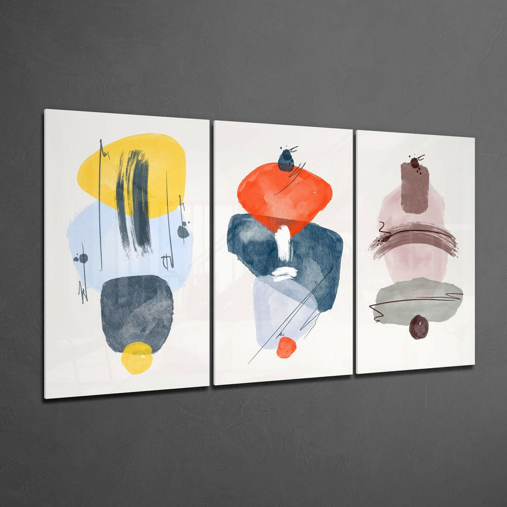 Three framed abstract glass wall art panels displaying geometric shapes in yellow, red, blue, brown, and pink tones against a gray wall.
