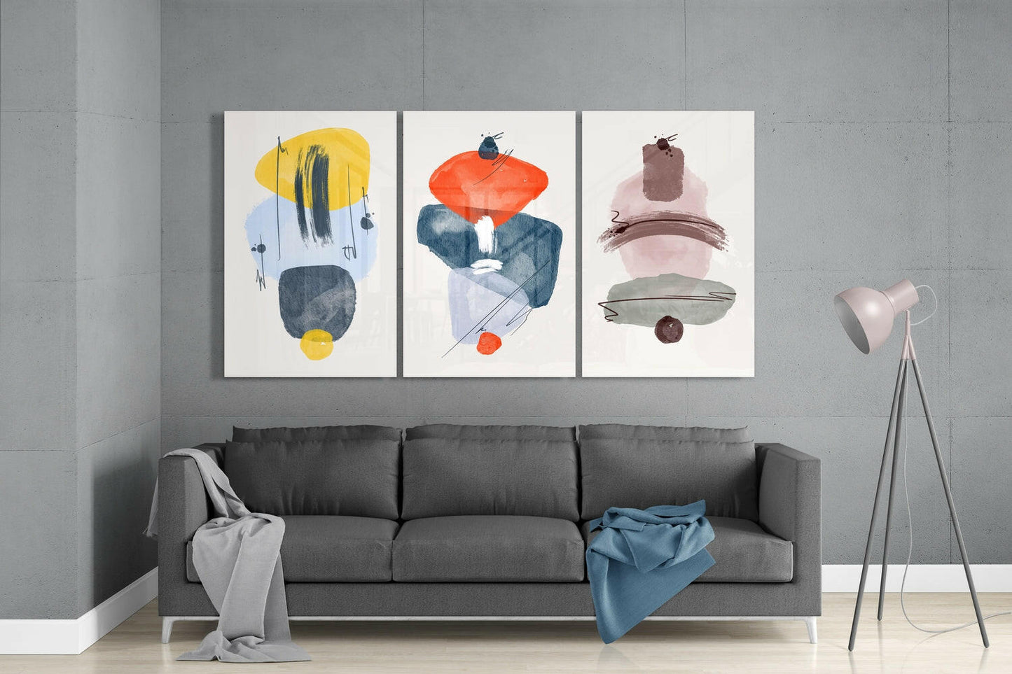 Three abstract glass wall art panels with geometric shapes in yellow, orange, pink, and navy displayed above a gray sofa in a modern interior.