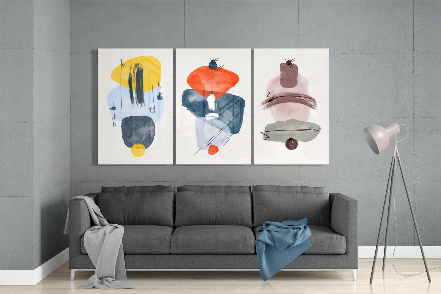 Three abstract glass wall art panels with geometric shapes in yellow, orange, pink, and navy displayed above a gray sofa in a modern interior.