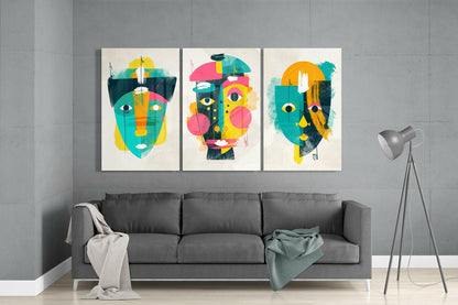 Three colorful abstract face artworks in teal, yellow, pink, and black displayed above a gray sofa in a modern living room.