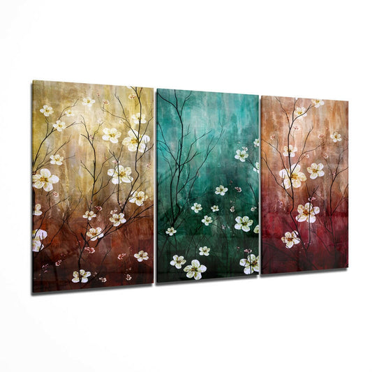 Three glass wall art panels displayed at an angle showing teal, gold, and rust backgrounds with white flowering branches.