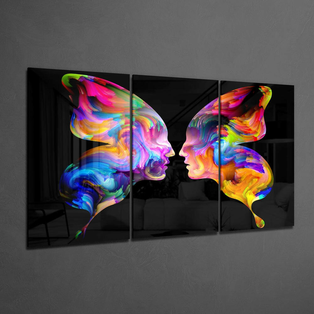Three-panel glass wall art displaying two colorful profile faces facing each other with vibrant rainbow swirls in pink, blue, yellow, and green on black background.
